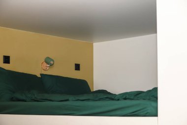 Modern, yer tasarruflu bir yatak odası solüsyonu, şık bir ranza ya da lambası ve temiz bir duvarı olan bir çatı katı yatak. Yeşil çarşaflı beyaz ranza. Rahat yatak odası..