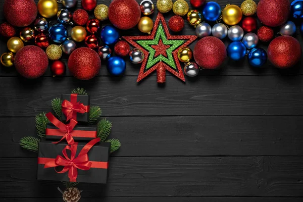 Concetto di Natale decorazione con nuove scatole regalo anno con nastro rosso, palle di Natale giocattoli, rami di abete, pigna su sfondo nero in legno con cornice per testo promozionale — Foto Stock