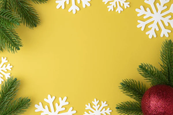 Fondo de Navidad con ramas de abeto, copo de nieve y juguete de año nuevo bola roja o bauble plano yacía sobre fondo pastel amarillo. Vista superior. Concepto mínimo — Foto de Stock