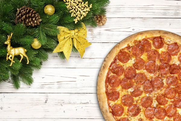 Pizza pepperoni Bożego Narodzenia śnieżynka z jodły oddziałów i nowy rok zabawka piłka, jelenia lub renifery, sosna stożek, łuk na stół biały deska drewno — Zdjęcie stockowe