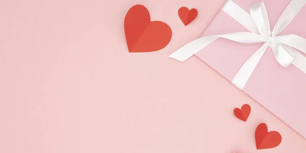 Ημέρα του Αγίου Βαλεντίνου ημέρα ιδέα σύνθεση: ροζ συσκευασία δώρου με λευκή κορδέλα και μικρές κόκκινες καρδιές σε χαρτί κοραλλιογενείς φόντο. Το Top view. Αγάπη μέρα έννοια επίπεδη θέσει — Φωτογραφία Αρχείου