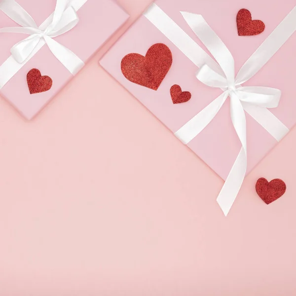 San Valentín idea composición: caja de regalo rosa con cinta blanca y pequeños corazones rojos sobre fondo de coral de papel. Vista superior. Amor día concepto plano laico — Foto de Stock