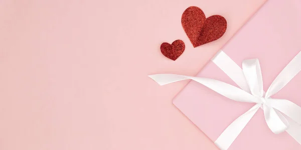День святого Валентина или женщин розовый подарок с белой лентой лук украшен красными маленькими сердцами на коралловом бумажном фоне. Концепция декора день любви или день рождения. Плоский лежал. Копирование пространства — стоковое фото