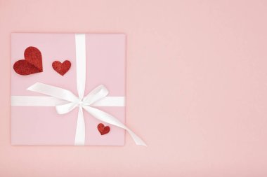 Sevgililer günü fikir kompozisyon: pembe hediye kutusu beyaz kurdele ve kağıt mercan arka plan üzerinde küçük kırmızı kalpler ile. Üstten görünüm. Aşk gün kavramı düz yatıyordu
