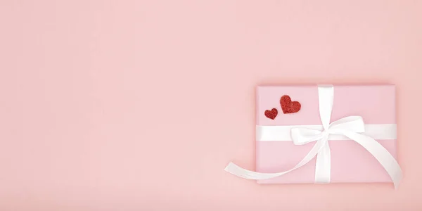 Состав идеи Дня Святого Валентина: розовая подарочная коробка с белой лентой и маленькие красные сердечки на бумажном коралловом фоне. Вид сверху. Концепция Дня любви — стоковое фото