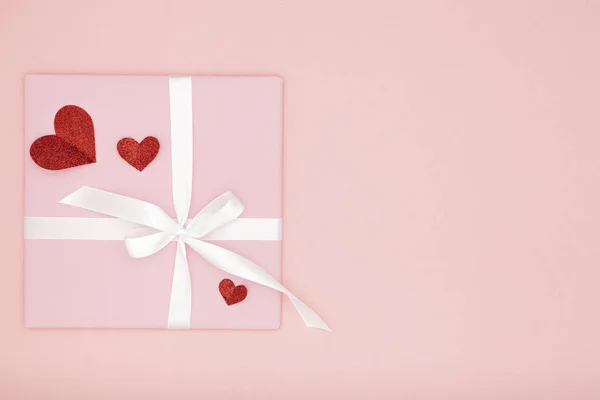Состав идеи Дня Святого Валентина: розовая подарочная коробка с белой лентой и маленькие красные сердечки на бумажном коралловом фоне. Вид сверху. Концепция Дня любви — стоковое фото