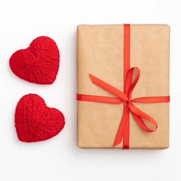 Día de San Valentín decoración en mesa escritorio vista superior. Composición plana de forma roja corazón y caja de regalo de papel artesanal con cinta de lazo rojo fondo blanco para maqueta de su diseño. Concepto de día de amor — Foto de Stock