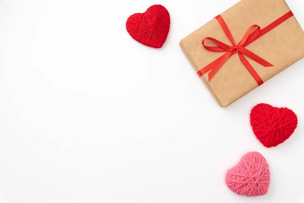 San Valentín idea composición: caja de regalo de papel artesanal con cinta roja y pequeños corazones rojos sobre fondo blanco. Vista superior. Amor día concepto plano laico — Foto de Stock