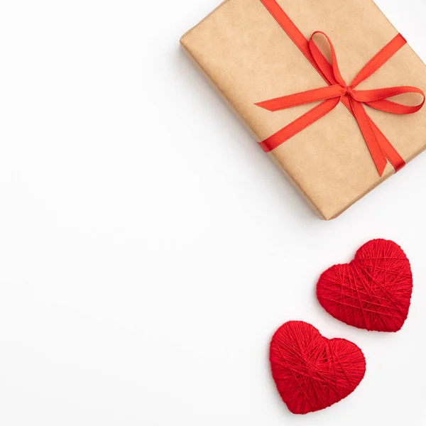 San Valentín idea composición: caja de regalo de papel artesanal con cinta roja y pequeños corazones rojos aislados sobre fondo blanco. Vista superior. Amor día concepto plano laico — Foto de Stock