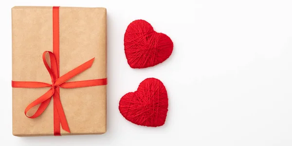 Decoración de San Valentín con caja de regalo de papel artesanal con cinta roja y pequeños corazones rojos aislados sobre fondo blanco. Vista superior. Amor día concepto plano laico — Foto de Stock