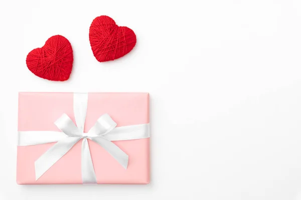 San Valentín idea composición: caja de regalo de color rosa o coral con cinta blanca y pequeños corazones rojos sobre fondo blanco. Vista superior. Amor día concepto plano laico — Foto de Stock