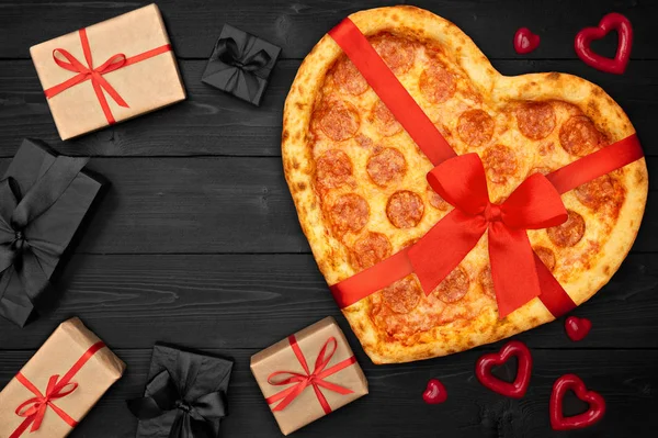 Pepperoni pizza ve tvaru srdce s červenou stuhou lukem a krabičce pro den svatého Valentýna na rustikální tmavé černé pozadí. Pohled shora. Rozložení bytu — Stock fotografie