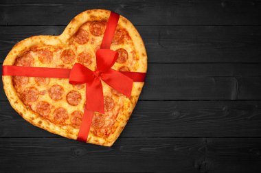 Rustik koyu siyah arka plan üzerinde kırmızı kurdele fiyonklu Sevgililer günü için kalp şeklinde biberli pizza. Üstten görünüm. Düz yatıyordu