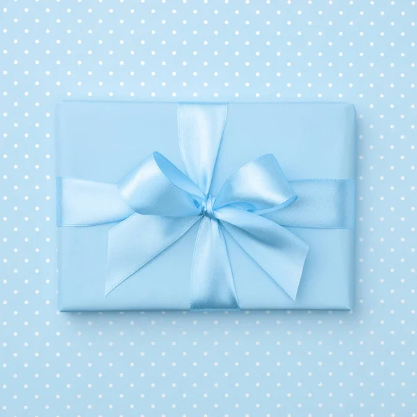 Gift box with blue ribbon bow on blue speckled background top view. Holiday concept, birthday gift, 8 march or Women day, gift box holiday Mothers day. Greeting card with copy space. Flat Lay