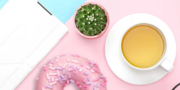 Escritorio de mesa de oficina plano con tablet computer, donut dulce, cactus, taza de té sobre fondo pastel rosa y azul. Vista superior. Espacio de trabajo doméstico de oficina — Foto de Stock