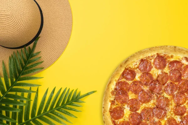 Pizza Pepperoni płaskie lay lato dekoracji wakacje ze słomką kapelusz, tropikalne liście palmowe na pastelowe żółte tło. Koncepcja letnia z kopią — Zdjęcie stockowe