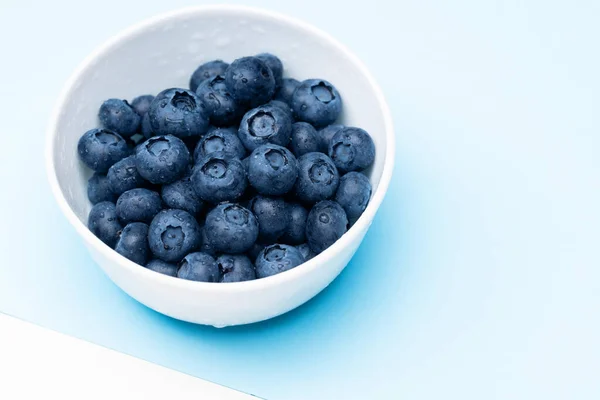 Mirtilo em tigela com gotas de água em um fundo azul . — Fotografia de Stock