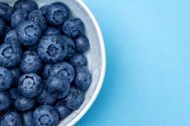 Mavi arka planda su damlaları olan yaban mersini kasesi.