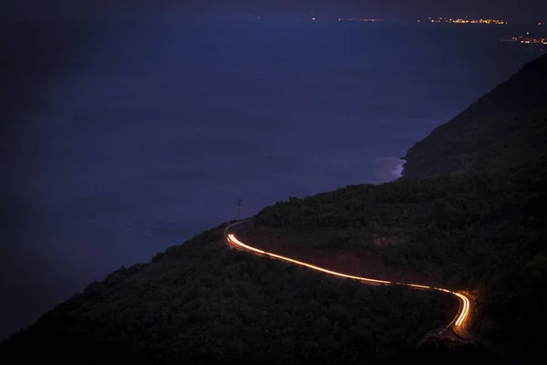A brightly lit road twisting and curving up a mountain in Long Exposure. The winding mountain road with light tracks from cars at the evening,