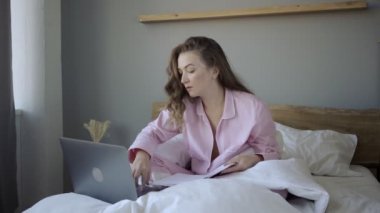 Dizüstü bilgisayarı ve not defteriyle yatakta gülümseyen serbest yazar.