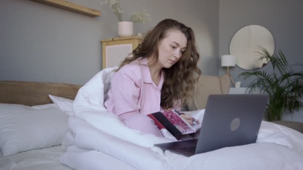 Freelancer sorridente com laptop e notepad na cama — Vídeo de Stock