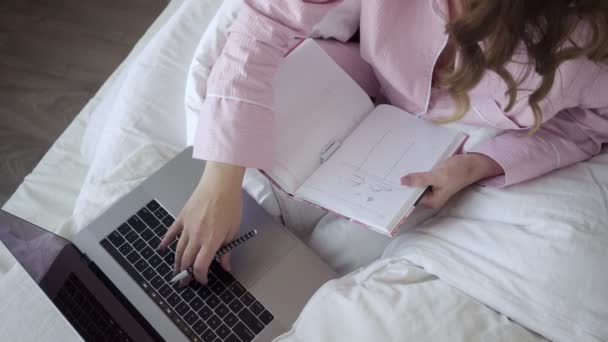 Lächelnde Freiberuflerin mit Laptop und Notizblock im Bett — Stockvideo