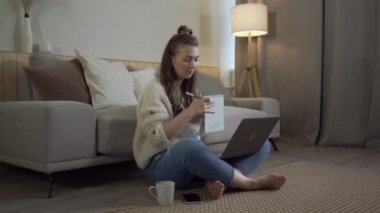 Netbook 'u halıya yapıştırmış odaklanmış bir kadın. Oturma odasında dizüstü bilgisayarla çalışan rahat bir serbest çalışan.