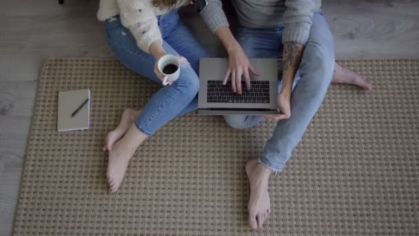 젊은 부부가 랩탑을 사용하여 거실 바닥에 앉아 있다. 거실에서 휴식을 취하고 있는 현대인 부부. — 비디오