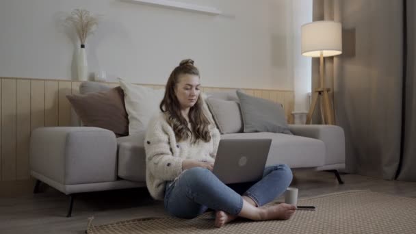 Gericht vrouw met netbook op tapijt. Ontspannen freelancer werkt op laptop in de woonkamer — Stockvideo