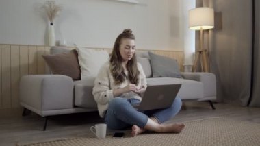 Netbook 'u halıya yapıştırmış odaklanmış bir kadın. Oturma odasında dizüstü bilgisayarla çalışan rahat bir serbest çalışan.