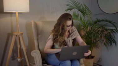 İşi için araştırma yapan genç bir kadın. Gülümseyen kadın kanepeye oturmuş online alışveriş sitesine göz gezdiriyordu. Evde boş zamanlarında internette gezinen mutlu kız..