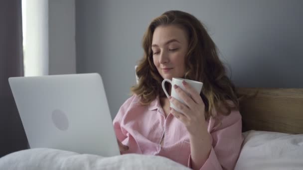 Woman with coffee using laptop in bed — Stock Video
