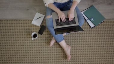 Netbook 'u halıya yapıştırmış odaklanmış bir kadın. Oturma odasında dizüstü bilgisayarla çalışan rahat bir serbest çalışan.