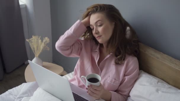 Woman with coffee using laptop in bed — Stock Video