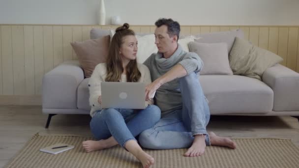 这对年轻夫妇用笔记本电脑在客厅的地板上休息。有笔记本电脑在客厅休息的当代夫妇. — 图库视频影像
