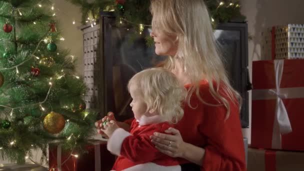 Feliz familia madre y bebé cerca del árbol de Navidad en la noche de vacaciones. — Vídeo de stock