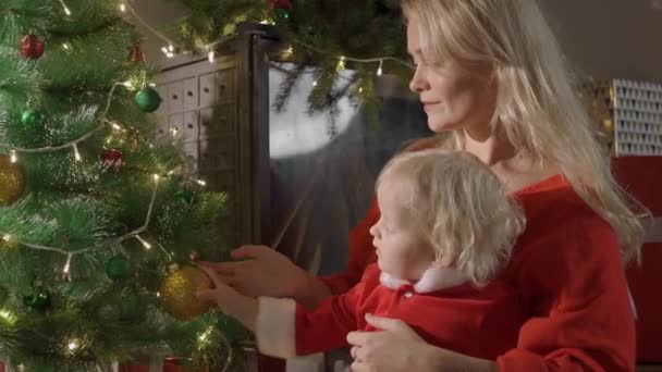 Feliz familia madre y bebé cerca del árbol de Navidad en la noche de vacaciones. — Vídeo de stock