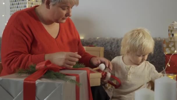 Ung mor binda båge på julklapp medan hennes dotter hjälpa henne de förbereder sig för semester hemma — Stockvideo