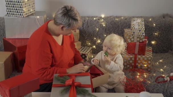 Ung mor binda båge på julklapp medan hennes dotter hjälpa henne de förbereder sig för semester hemma — Stockvideo