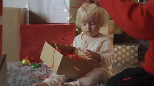 Joven madre atando arco en regalo de Navidad mientras su hija le ayuda a prepararse para las vacaciones en casa — Vídeo de stock