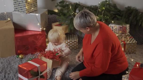 Ibu muda mengikat busur pada hadiah Natal sementara putrinya membantu dia mereka mempersiapkan diri untuk liburan di rumah — Stok Video
