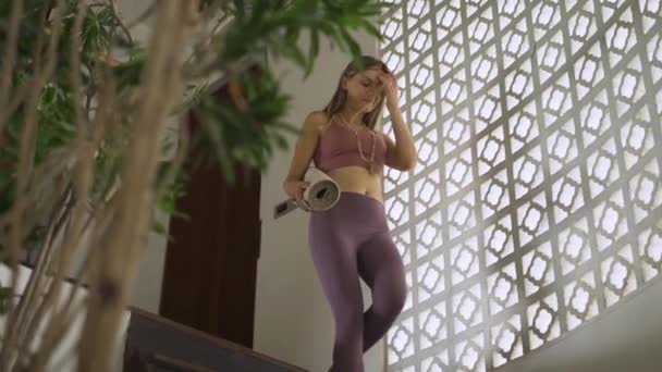 Mladá žena ve sportovním oblečení drží doma podložku na jógu. — Stock video
