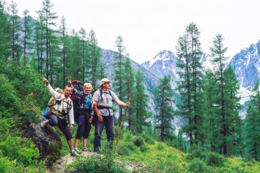 Turistler güneşli bir günde kozalaklı ormanın arkasındaki karlı dağlara karşı taş üzerinde durmak. Dağlık arazide yürüyüş. Shavlinsky göllerinde buzula giden yol, Altay, 31 Temmuz 2018.