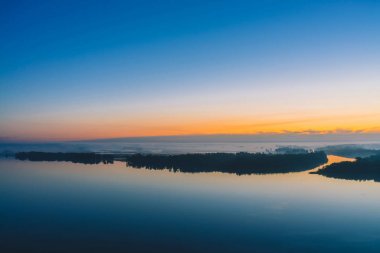 Geniş nehir kalın sis altında orman ile diyagonal kıyı boyunca akar. Erken mavi gökyüzü suya yansıdı. Pitoresk şafak öncesi gökyüzünde sarı parıltı. Görkemli doğanın renkli sabah atmosferik manzara