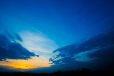Şehir binalarının siluetleri arkasında atmosferik mavi bulutlu gökyüzü. Kobalt ve kopya alanı için yoğun bulutlar ve parlak sarı güneşli ışık ile gündoğumu turuncu arka plan. Bulutların üzerindeki Siyam cenneti.