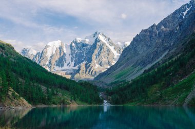Muhteşem, dev, karlı dağlar. Nehir buzuldan dağ gölüne akar. Dağlık bölgelerdeki suda yansıma. Tepede beyaz kar var. Muhteşem atmosferik doğa manzarası..
