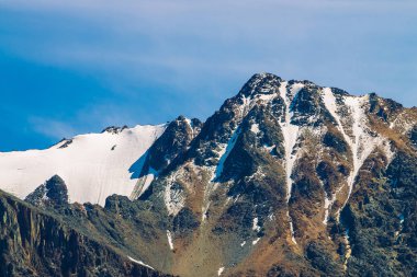 Mavi berrak gökyüzünde karlı dağ tepesinde. Güneşli bir günde bulutların altında kayalık sırt. Görkemli doğanın atmosferik minimalist manzara.