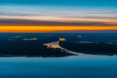 Şafak öncesi gökyüzünün altında ağaçlar ile büyük ada ile güzel nehir. Pitoresk bulutlu gökyüzünde parlak turuncu şerit. Erken mavi gökyüzü suya yansıdı. Görkemli doğanın renkli sabah atmosferik görüntüsü.
