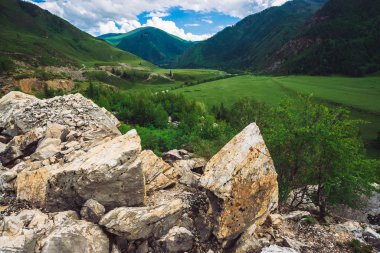 Orman güneş ışığıyla kaplı harika dağlar. Büyük taşlardaki boşluğu kopyalayın. Güneşli bir günde dağlık arazide zengin bir bitki örtüsü. Nehir ve karayolu ile görkemli bir dağ manzarası.