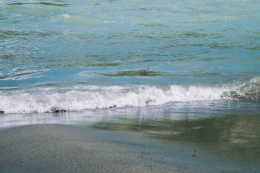 Turkuaz akan su yüzeyi ve kum detaylı doku. Dağ nehrinin akıntıları yaklaşıyor. Sahilde temiz su dalgalarının arka planı.